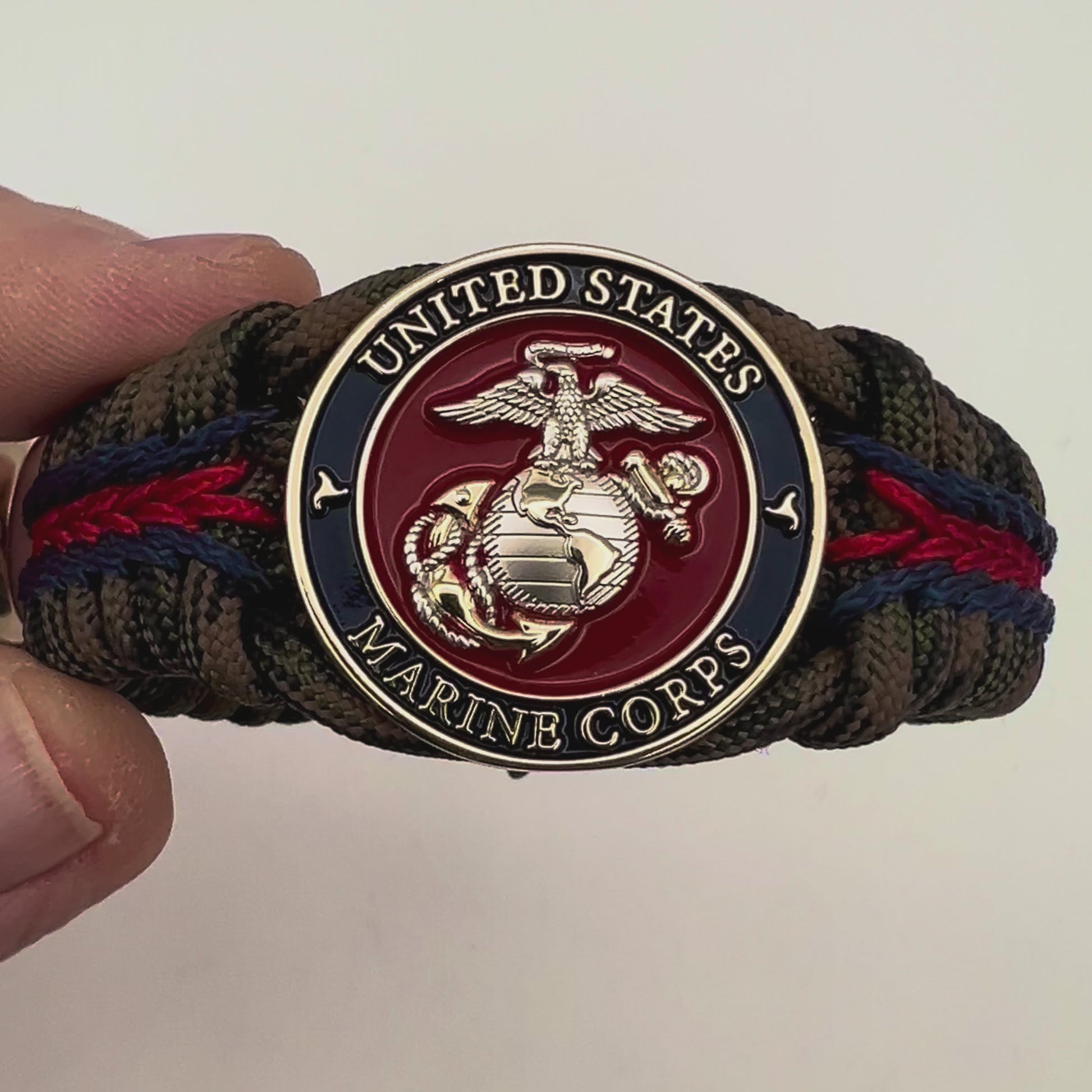 Thick, semi-rigid and comfortable braided United States Marine Corps bracelet featuring a 24K gold and silver plated USMC officer Eagle Globe and Anchor medallion, a gold Cobra style tactical buckle and woven with Woodland Camo 550 paracord and Imperial Red and Navy Blue micro cord.