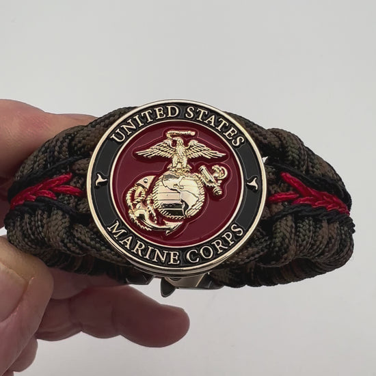 Thick, semi-rigid and comfortable braided United States Marine Corps bracelet featuring a 24K gold plated USMC Eagle Globe and Anchor medallion, a gold Cobra style tactical buckle and woven with Woodland camo 550 paracord and black and Imperial red micro cord.