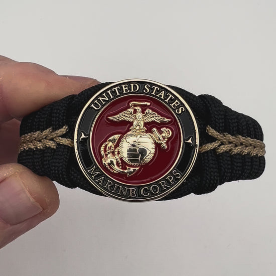 Thick, semi-rigid and comfortable braided United States Marine Corps bracelet featuring a 24K gold plated USMC officer Eagle Globe and Anchor medallion, a black Cobra style tactical buckle and woven with black 550 paracord and gold micro cord.
