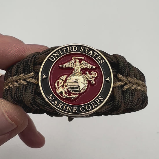 Thick, rigid and comfortable braided United States Marine Corps bracelet featuring a 24K gold plated USMC Eagle Globe and Anchor medallion, a gold Cobra style tactical buckle and woven with Woodland 550 paracord.