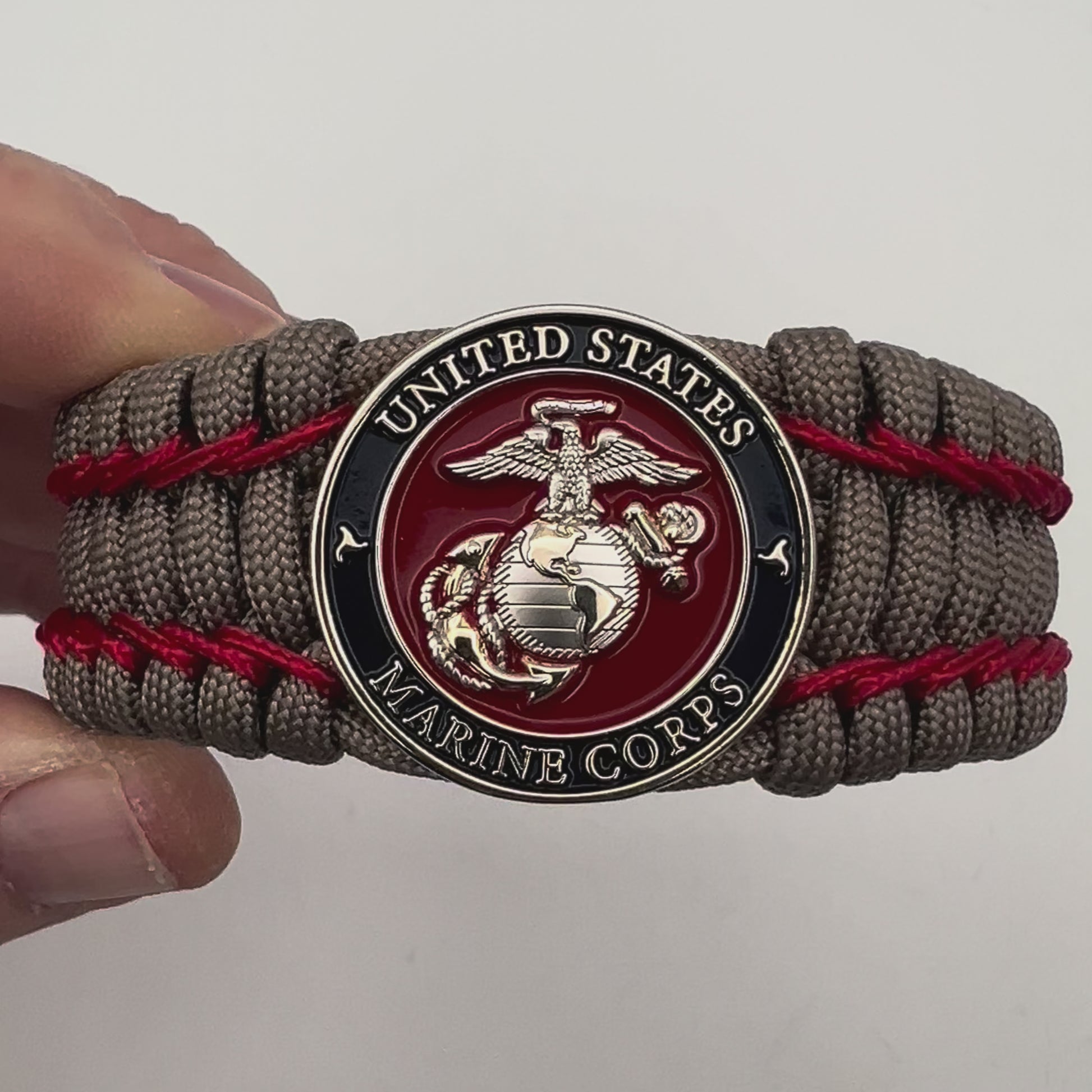 Thick, semi-rigid and comfortable braided United States Marine Corps bracelet featuring a 24K gold and silver plated USMC officer Eagle Globe and Anchor medallion, a gold Cobra style tactical buckle and woven with tan 550 paracord and Imperial Red micro cord.