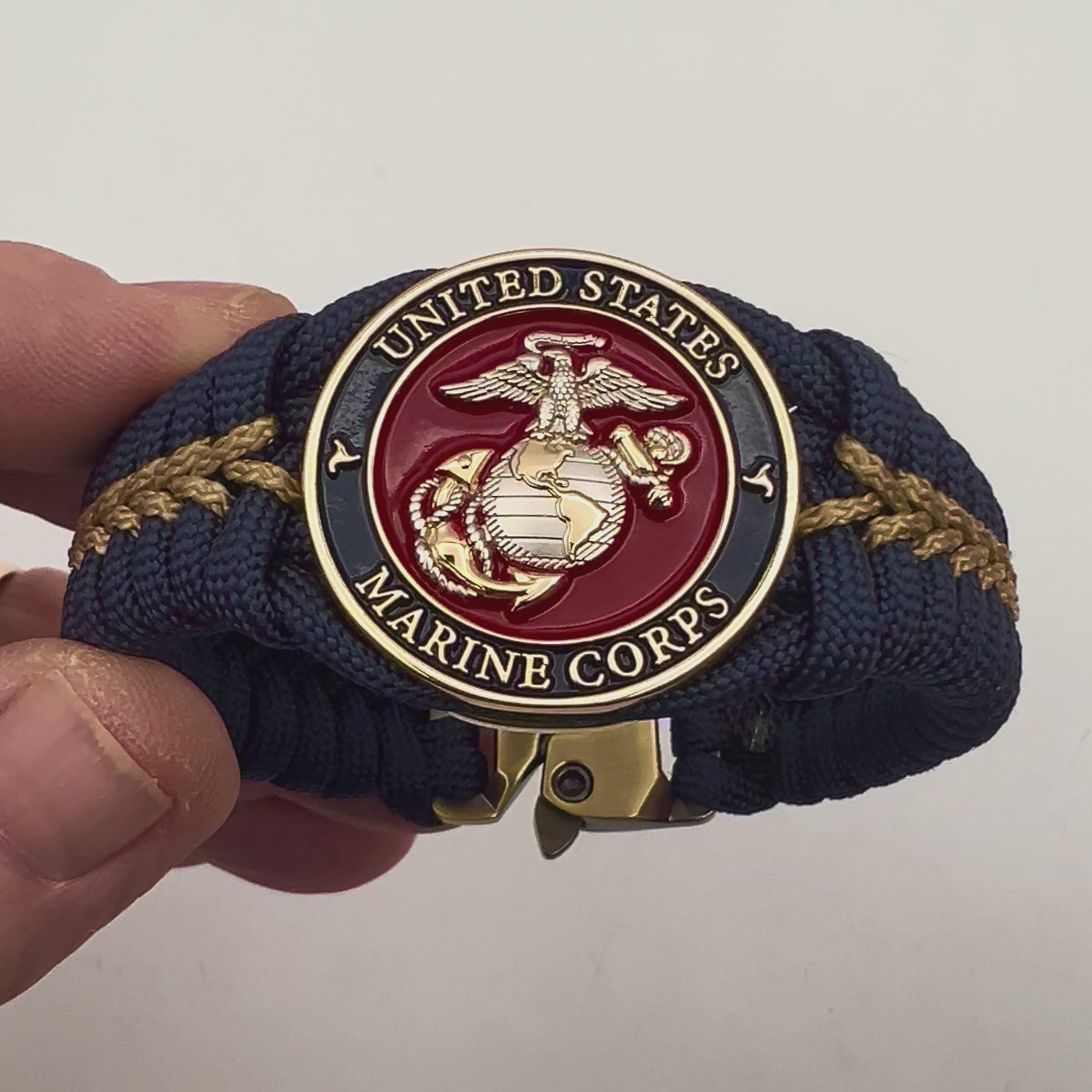 Thick and comfortable braided United States Marine Corps bracelet featuring a 24K gold and silver plated USMC officer Eagle Globe and Anchor medallion, a Cobra style tactical buckle and woven with Navy blue and gold paracord.
