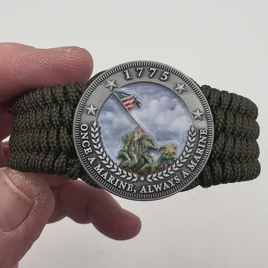 Thin, wide, flexible and comfortable braided United States Marine Corps Iwo Jima bracelet featuring an antique silver plated UV painted Iwo Jima flag raising medallion, a silver Cobra style tactical buckle and woven with olive drab Type-1 paracord.