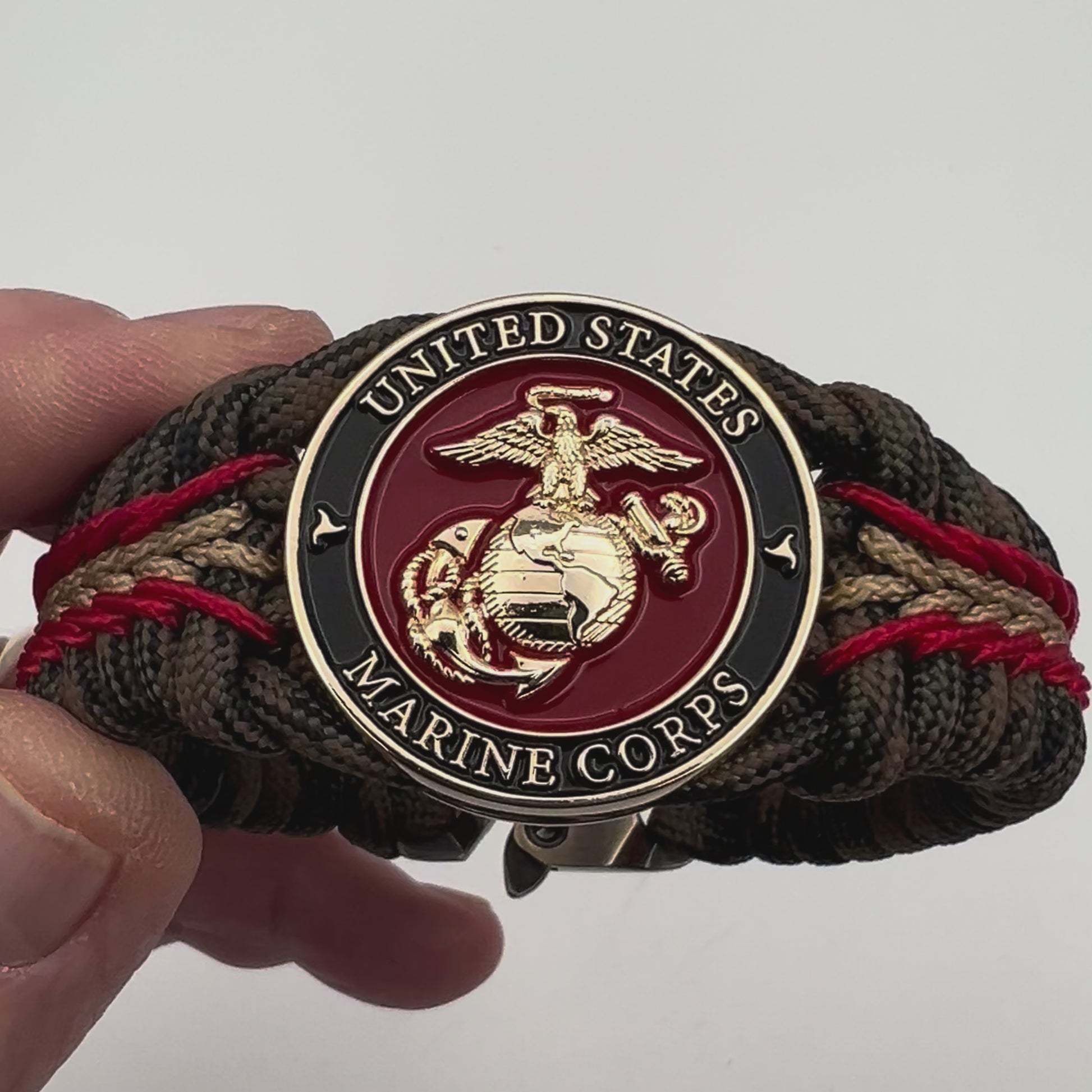 Thick, rigid and comfortable braided United States Marine Corps bracelet featuring a 24K gold plated USMC Eagle Globe and Anchor medallion, a gold Cobra style tactical buckle and woven with Woodland camo 550 paracord and Imperial Red and Gold micro cord.