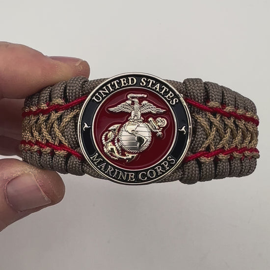 Thick, semi-rigid and comfortable braided United States Marine Corps bracelet featuring a 24K gold and silver plated USMC officer Eagle Globe and Anchor medallion, a gold Cobra style tactical buckle and woven with tan 550 paracord and Imperial Red and gold micro cord.