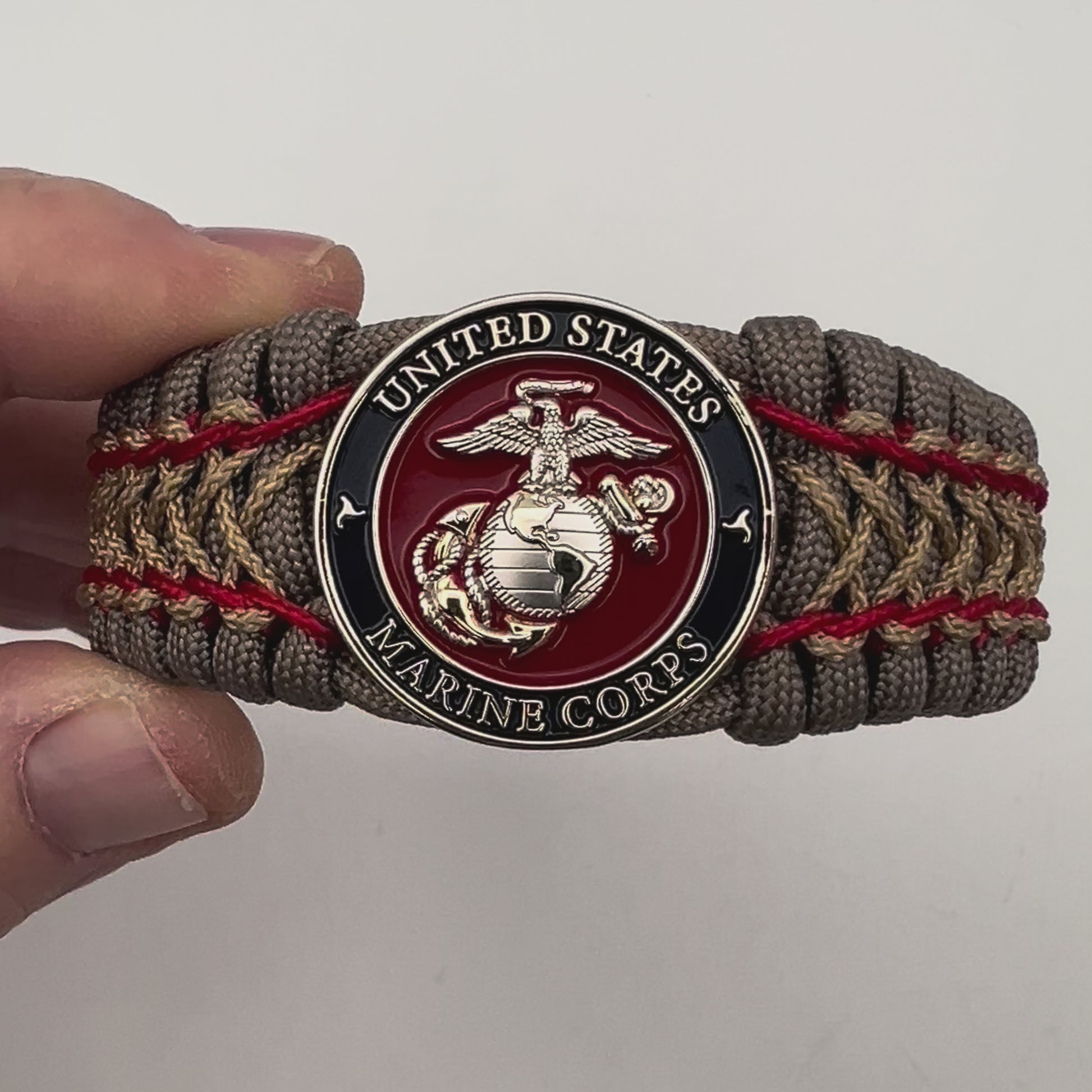 Thick, semi-rigid and comfortable braided United States Marine Corps bracelet featuring a 24K gold and silver plated USMC officer Eagle Globe and Anchor medallion, a gold Cobra style tactical buckle and woven with tan 550 paracord and Imperial Red and gold micro cord.
