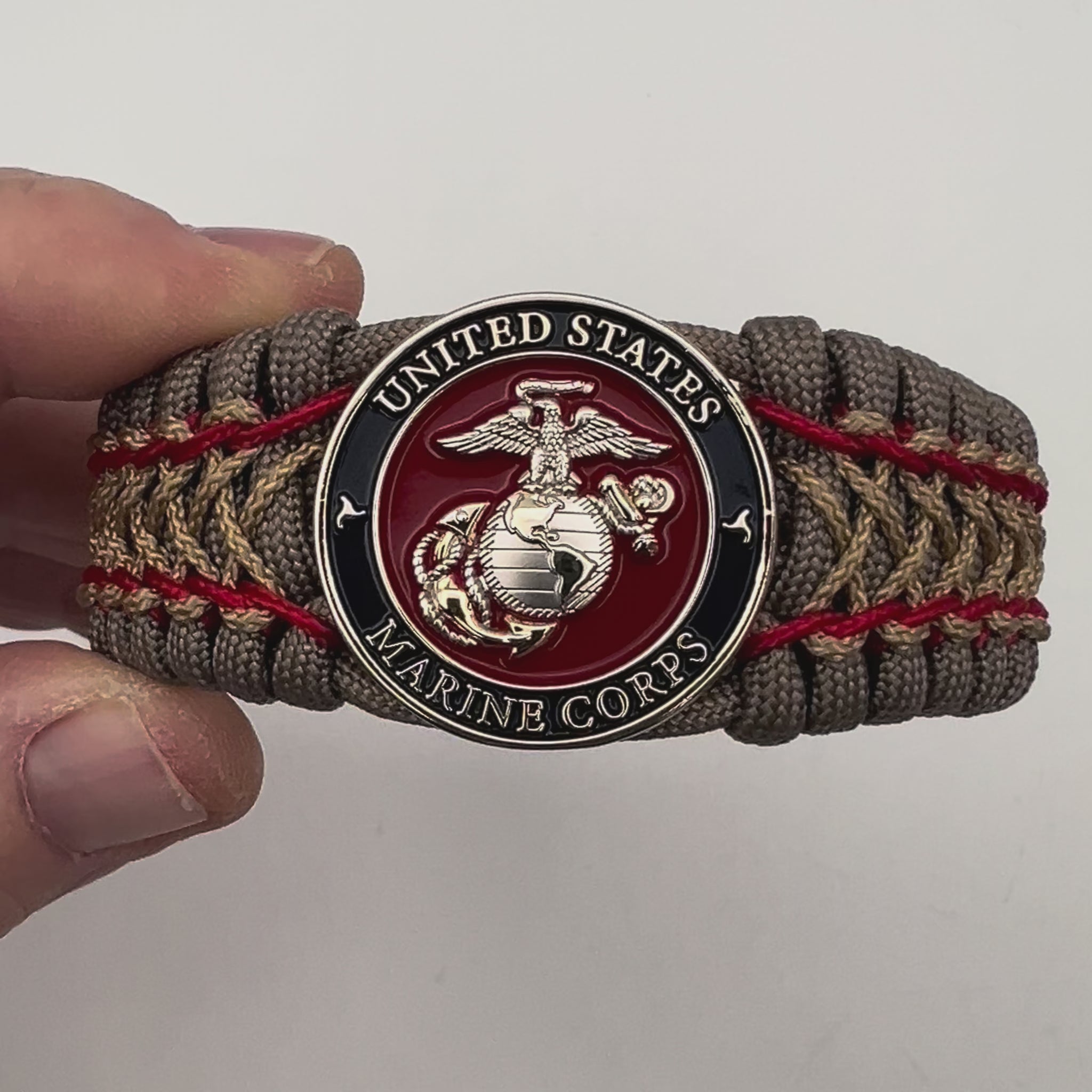 Thick, semi-rigid and comfortable braided United States Marine Corps bracelet featuring a 24K gold and silver plated USMC officer Eagle Globe and Anchor medallion, a gold Cobra style tactical buckle and woven with tan 550 paracord and Imperial Red and gold micro cord.