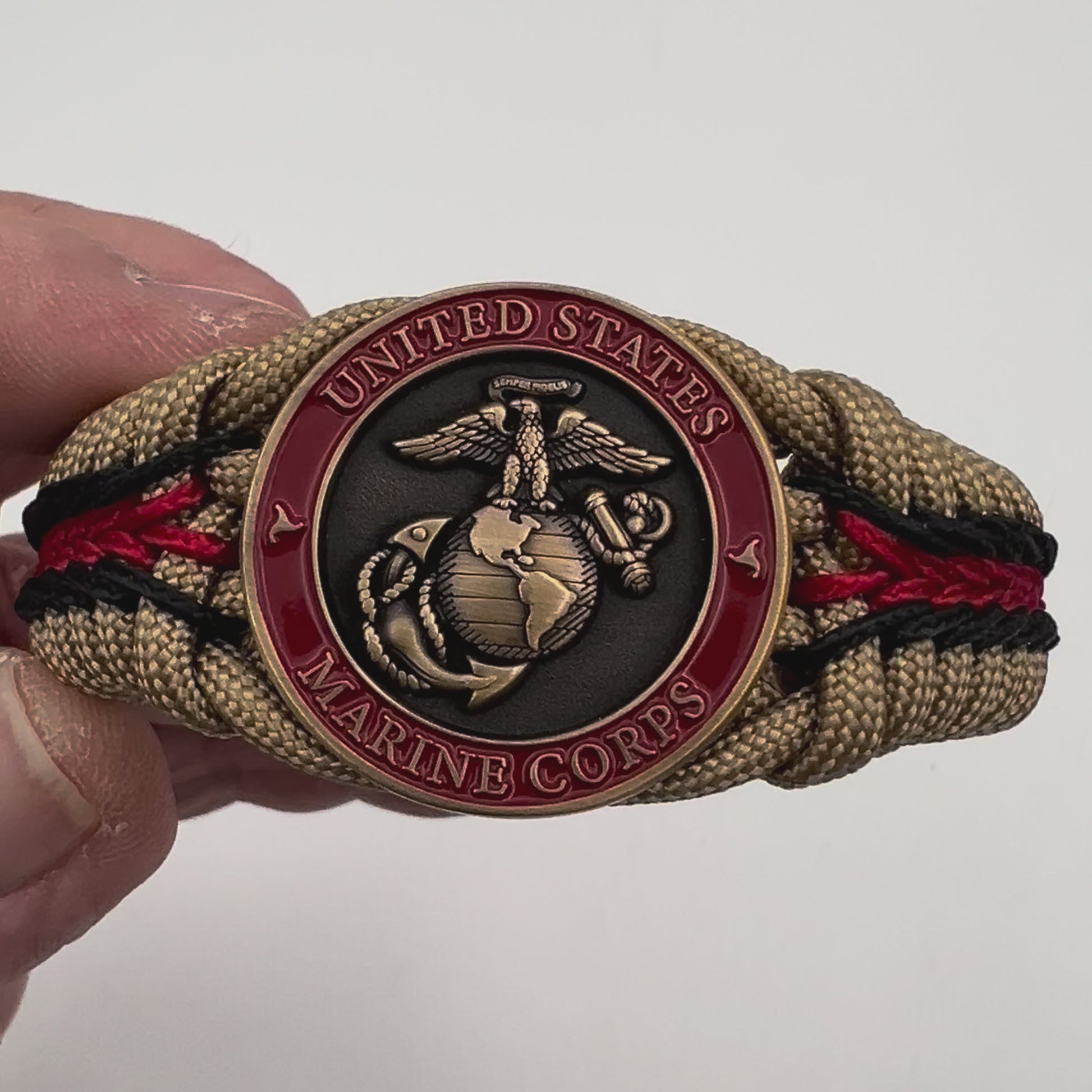 Thick, medium width, rigid and comfortable braided United States Marine Corps bracelet featuring a 24K antique gold plated USMC Eagle Globe and Anchor medallion, a gold Cobra style tactical buckle and woven with gold 550 paracord and Imperial red and black micro cord.