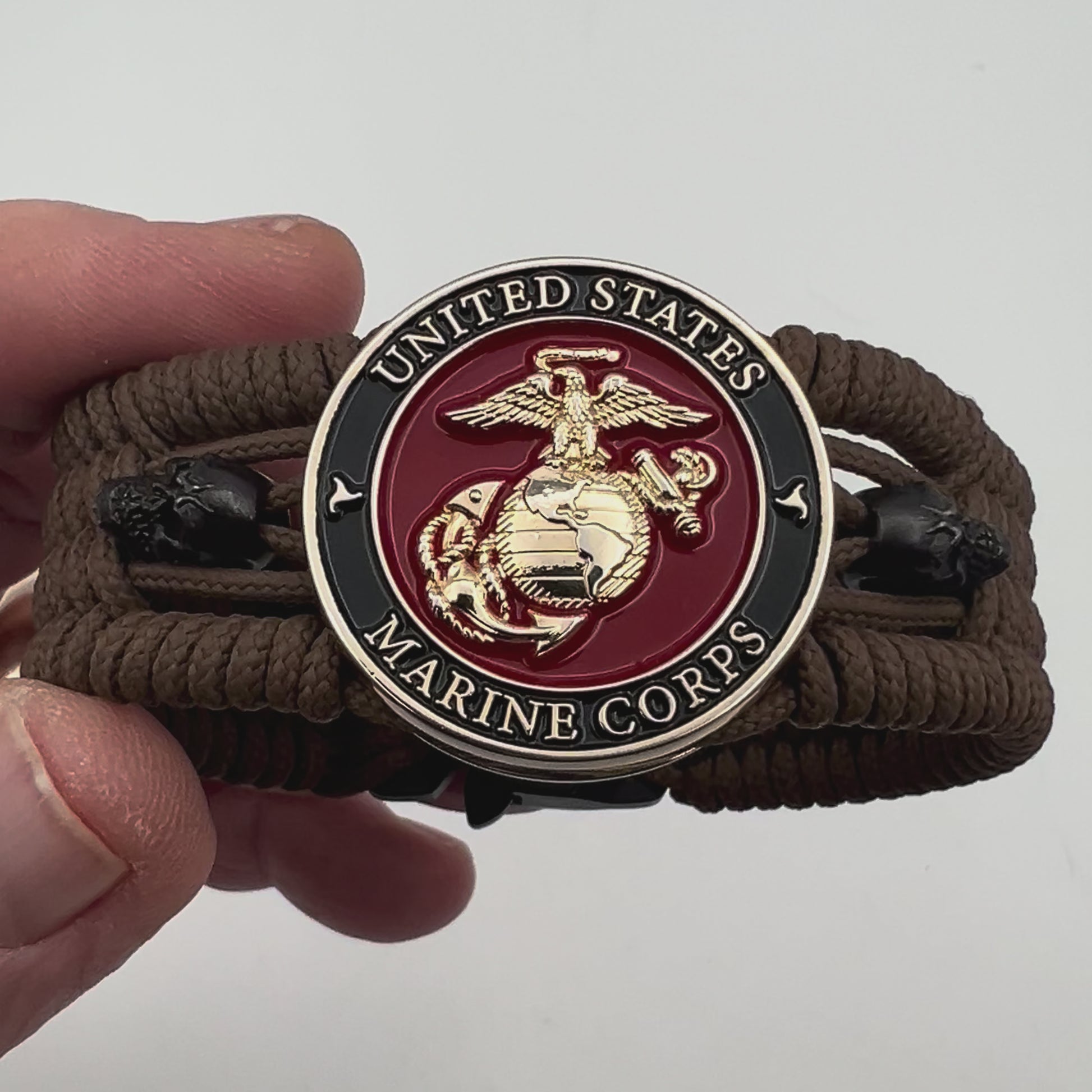 Thin, medium width, flexible and comfortable braided United States Marine Corps bracelet featuring a 24K gold plated USMC officer Eagle Globe and Anchor medallion, two black micro skulls, a black Cobra style tactical buckle and woven with Coyote Brown Type-1 paracord.