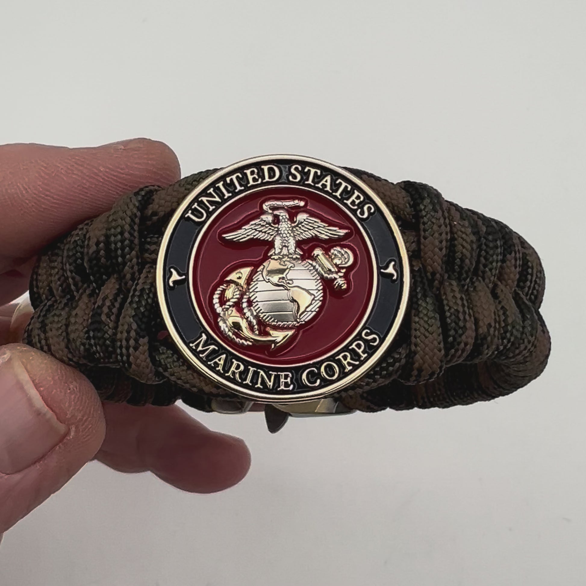 Thick, semi-rigid and comfortable braided United States Marine Corps bracelet featuring a 24K gold and silver plated USMC officer Eagle Globe and Anchor medallion, a gold Cobra style tactical buckle and woven with Woodland Camo 550 paracord.