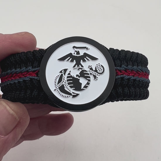 Thin, medium width, flexible and comfortable braided United States Marine Corps bracelet featuring a black USMC Eagle Globe and Anchor medallion, a black Cobra style tactical buckle and woven with black Type-1 paracord and stitched with red and blue nano cord.