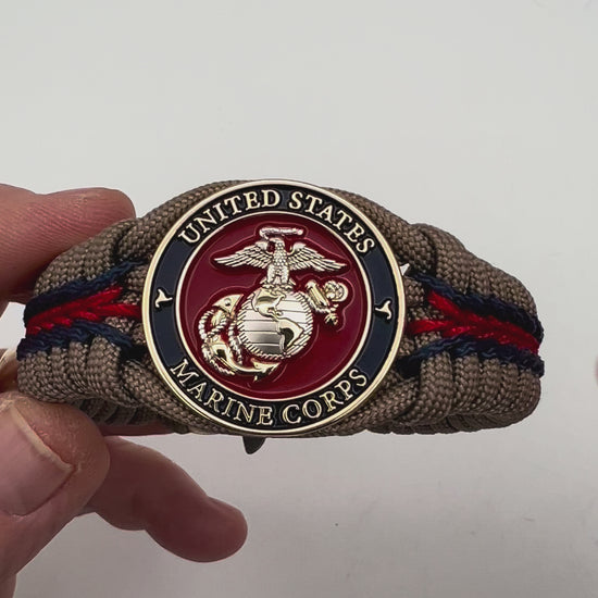 Thick, semi-rigid and comfortable braided United States Marine Corps bracelet featuring a 24K gold and silver plated USMC officer Eagle Globe and Anchor medallion, a gold Cobra style tactical buckle and woven with tan 550 paracord and Imperial red and gold micro cord.
