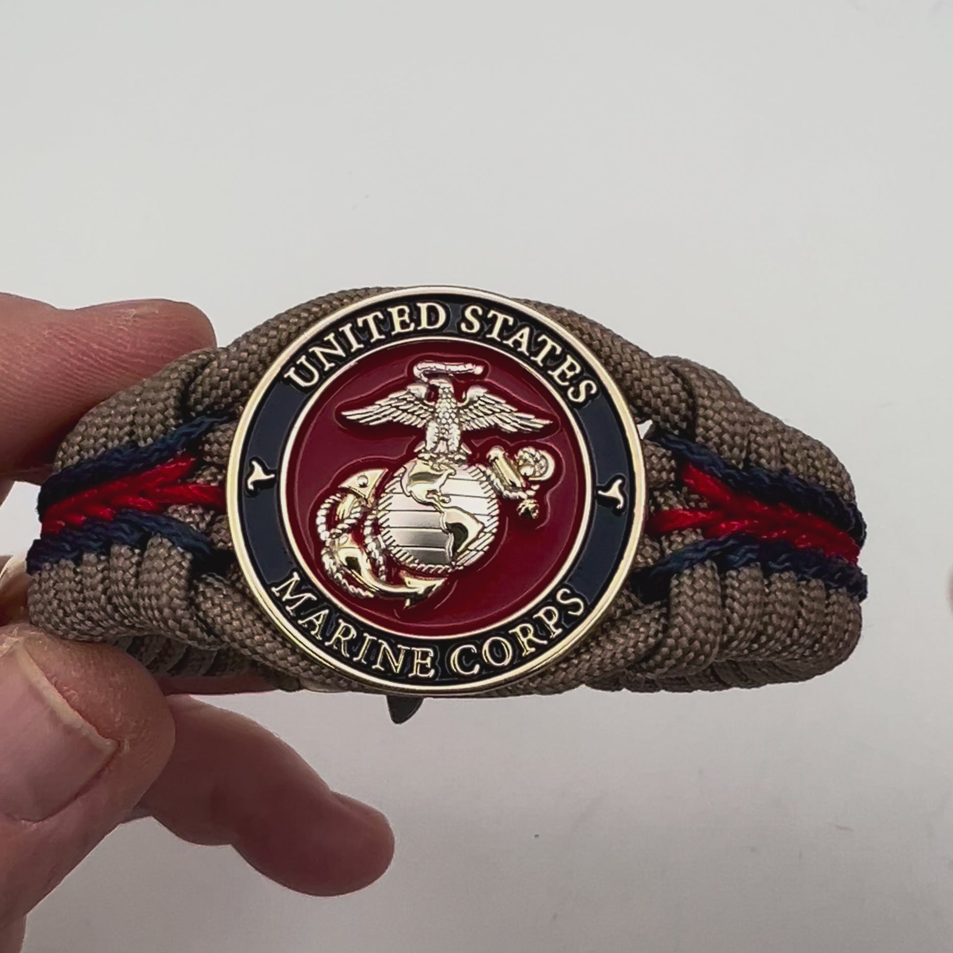Thick, semi-rigid and comfortable braided United States Marine Corps bracelet featuring a 24K gold and silver plated USMC officer Eagle Globe and Anchor medallion, a gold Cobra style tactical buckle and woven with tan 550 paracord and Imperial red and gold micro cord.